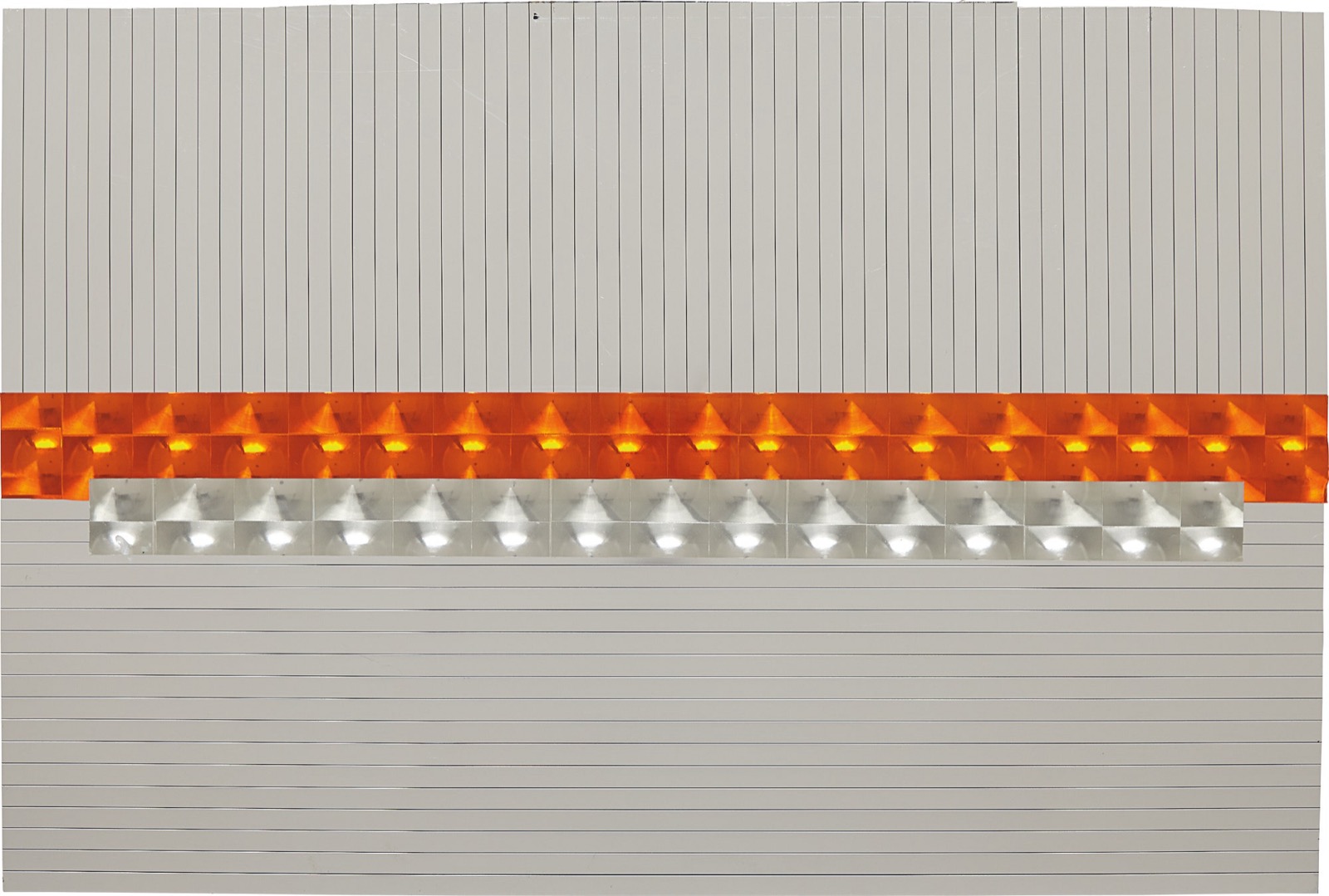 A wall panel of grey striped metal crossed by a band of orange reflector cells, with a silver band of the same cells set below and to the right, photographed under flat grey light.