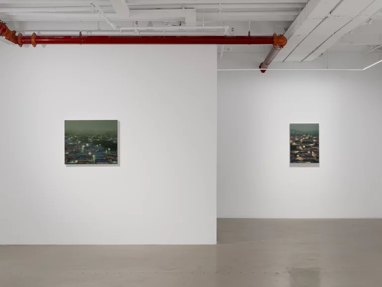 Two small Youngju Joung paintings of lit hillside villages hung far apart on white walls in a Tribeca gallery with a red sprinkler pipe overhead.