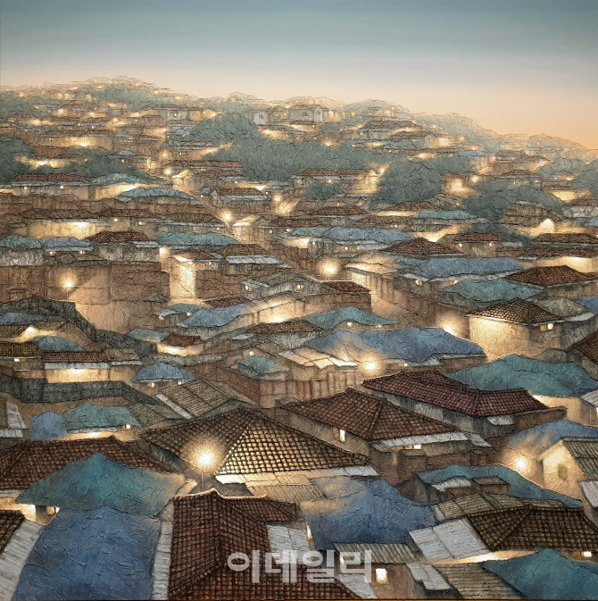 Blue and brown tiled roofs stacked up a hillside at dusk, lamps and windows glowing, painted in torn layers of hanji paper.