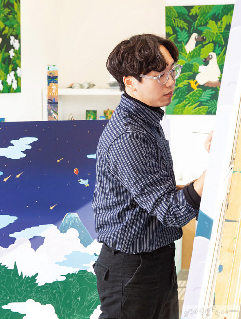Kim Sunwoo standing at an easel in his studio, working on a canvas, with finished dodo paintings on the wall and floor behind him.