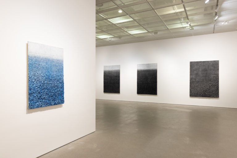 Installation view of four Lee Jinwoo paintings on white gallery walls. The nearest, on its own wall, is blue and white. The three beyond it are black fading to white at the top.